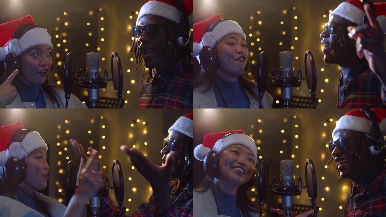 在录音棚里用圣诞老人帽子录制的两位不同歌手的特写肖像。年轻的黑人男性和亚洲女性艺术家在背景中与圣诞灯