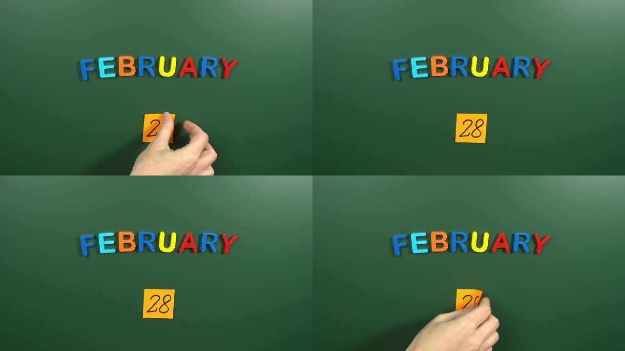 2月28日日历日用手在学校董事会上贴一张贴纸。28 2月日期。2月第二十八天。第28个日期号。28天