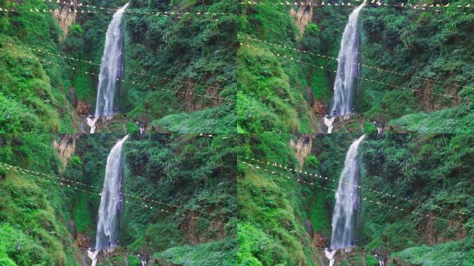 大瀑布的视差从陡峭的悬崖附近郁郁葱葱的绿色景观沿安纳普尔纳电路徒步旅行在尼泊尔。经幡在前景中缓缓飘扬