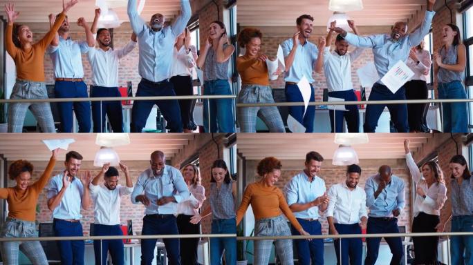 商业团队在多元文化办公室庆祝，同事将文书工作抛向空中