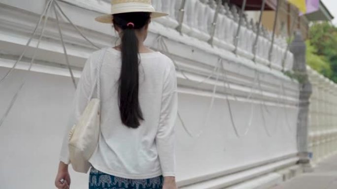 享受曼谷旅游目的地亚洲女性旅游地标的旅行者。泰国曼谷，一名女游客拖着行李箱在寺庙墙Wat Phra 