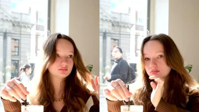 十几岁的女孩在一家餐厅的咖啡馆里喝一杯冷拿铁咖啡，背景是索尼阳光明媚的天气棕色夹克长长的飘逸的头发沉