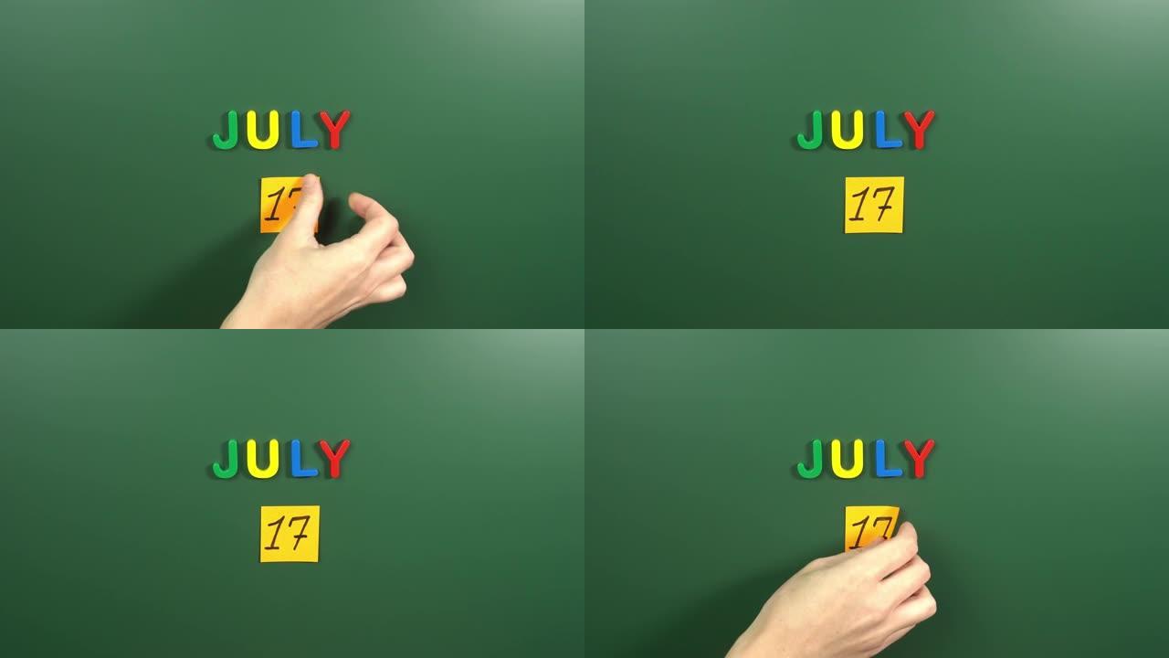 7月17日日历日用手在学校董事会上贴一张贴纸。17 7月日期。7月的第十七天。第17个日期编号。17