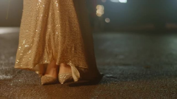 女人脚穿着豪华闪亮的金鞋和连衣裙在晚上慢慢走