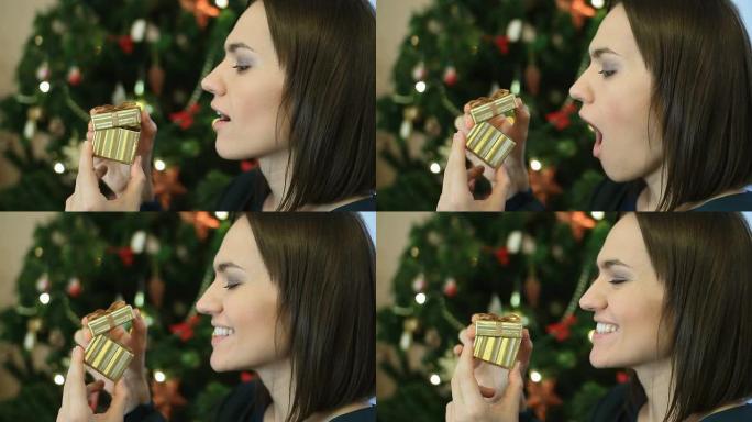 快乐兴奋的女人打开礼品盒，背景中的圣诞树