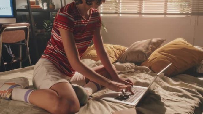 清晨，卷曲的年轻女孩坐在床上在笔记本电脑上打字