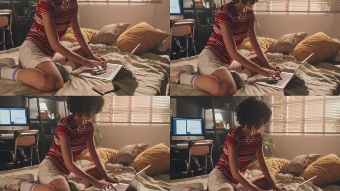 清晨，卷曲的年轻女孩坐在床上在笔记本电脑上打字