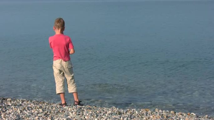 小男孩站在海滩上，向大海扔石头