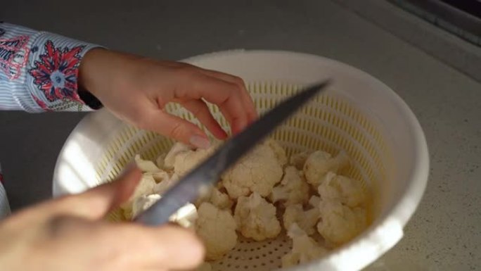 关闭女人在厨房手工烹饪清洁花椰菜，用刀在切菜板上切割戴着头巾的食品。在家中的伊斯兰女性。家庭主妇日常