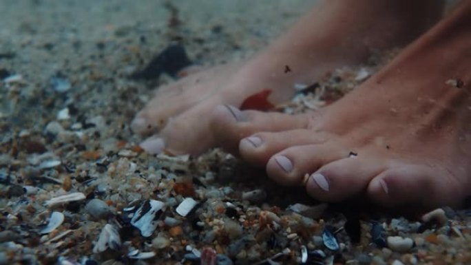 特写女人的脚在水下扭动脚趾，享受温和的海滩海沙溅水站在贝壳上