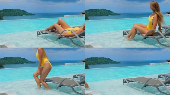 穿着泳衣的性感女人从日光浴躺椅上站起来，离开蓝色游泳池