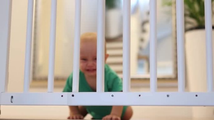 限制概念哭泣的婴儿小孩绿色衬衫爬在白色栅栏后面