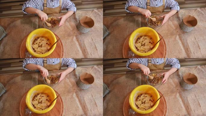 一个可爱的儿童面包师糖果的俯视图，用葡萄干搅拌糖，帮助妈妈烹饪复活节蛋糕或panettone