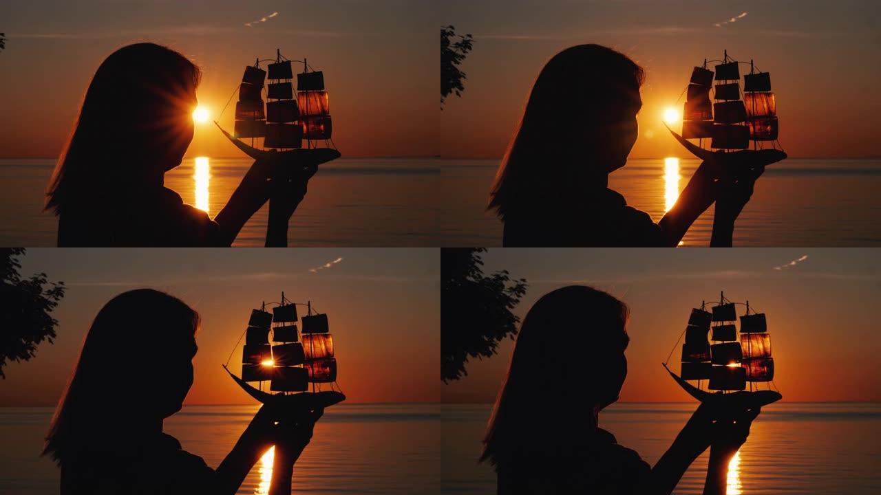 日落时分，一个女人站在海边，手里拿着一艘帆船的模型。希望与旅游理念