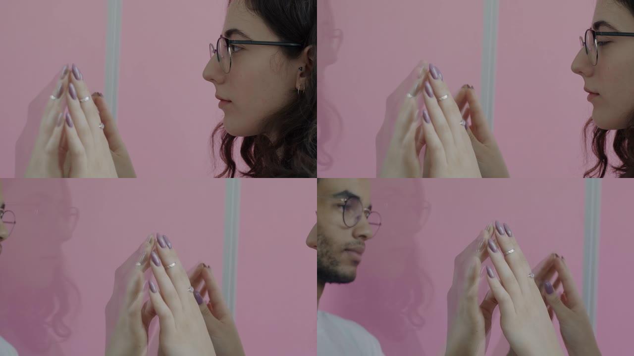 男女混血儿夫妇的慢动作穿过粉红色背景的玻璃墙触摸手
