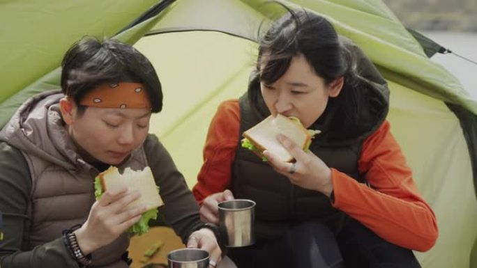 两名亚洲女性游客在户外帐篷入口共进午餐