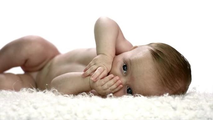 一个婴儿侧躺着，用手在嘴里玩耍