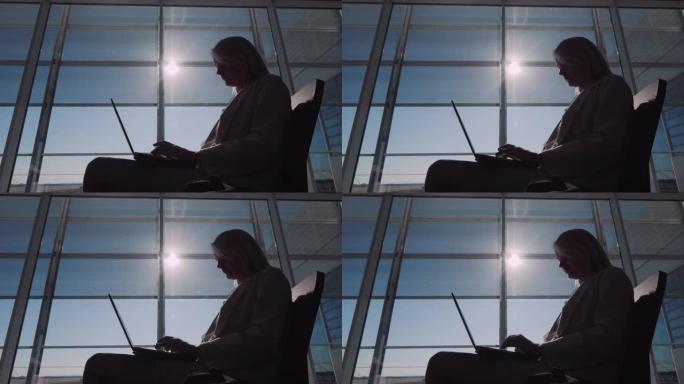 一名年轻的女商人用笔记本电脑在机场大厅等待航班的剪影