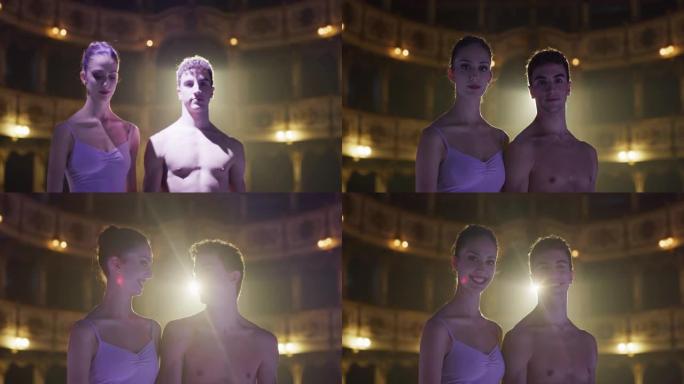 年轻的芭蕾舞演员夫妇在经典剧院里看着镜头，带着戏剧性的灯光微笑的电影镜头。专业男女舞蹈表演者自信行走