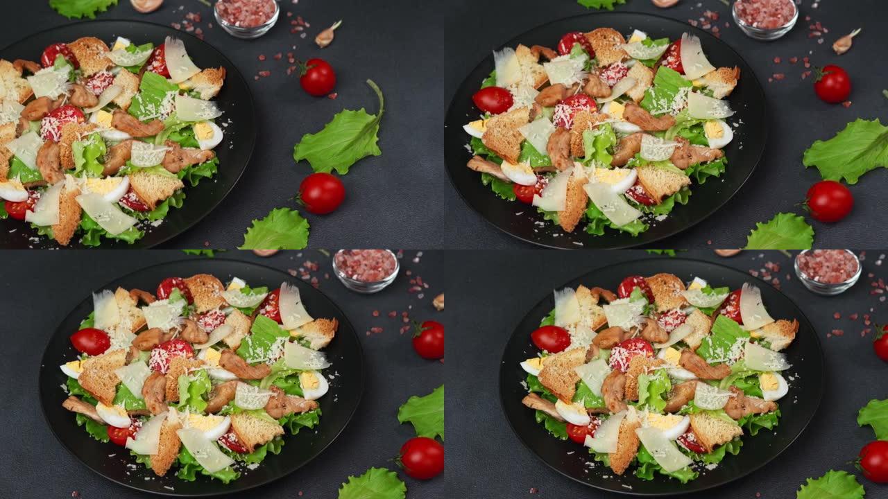 凯撒沙拉与鸡肉，莴苣叶，樱桃番茄，磨碎的帕尔马干酪在黑色背景下的黑色盘子中的特写镜头