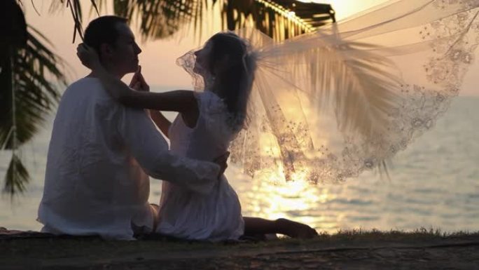婚礼情侣拥抱在棕榈枝下对抗海洋