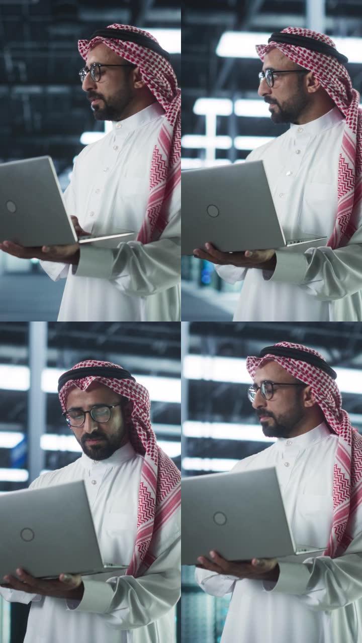 垂直屏幕: 中东IT系统工程师穿着传统的白色长袍，在现代技术服务器农场设施中使用笔记本电脑。工作中的