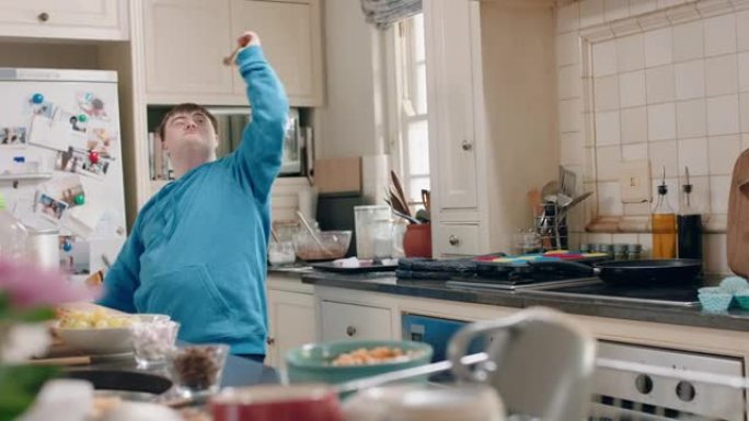 患有唐氏综合症的快乐十几岁的男孩在厨房跳舞，开心地庆祝有趣的舞蹈，享受周末在家