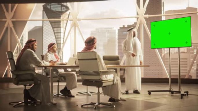 多元化的穆斯林办公室会议室: 中东首席执行官为企业家做演讲，交谈，使用带有绿屏模拟显示的电视。商人谈