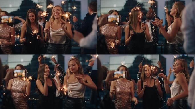 美丽的年轻女子跳舞与烟火女友庆祝新年前夜在迷人的派对穿着时尚时尚的朋友使用智能手机分享庆祝视频在社交