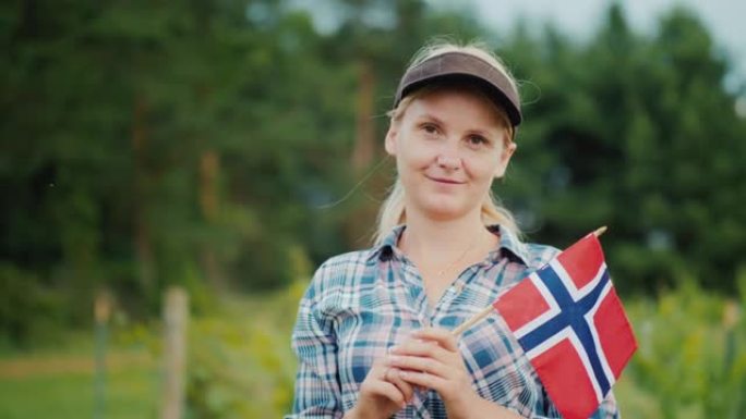 一个挂着挪威国旗的女人站在花园旁。挪威农民