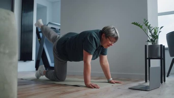 老年妇女在家做体育锻炼，双手和膝盖站立，观看在线锻炼