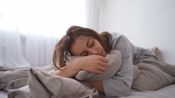 年轻女子独自躺在家里的床上，又冷又病。疾病，感冒，病毒，在家打电话给医生，电话咨询医生。