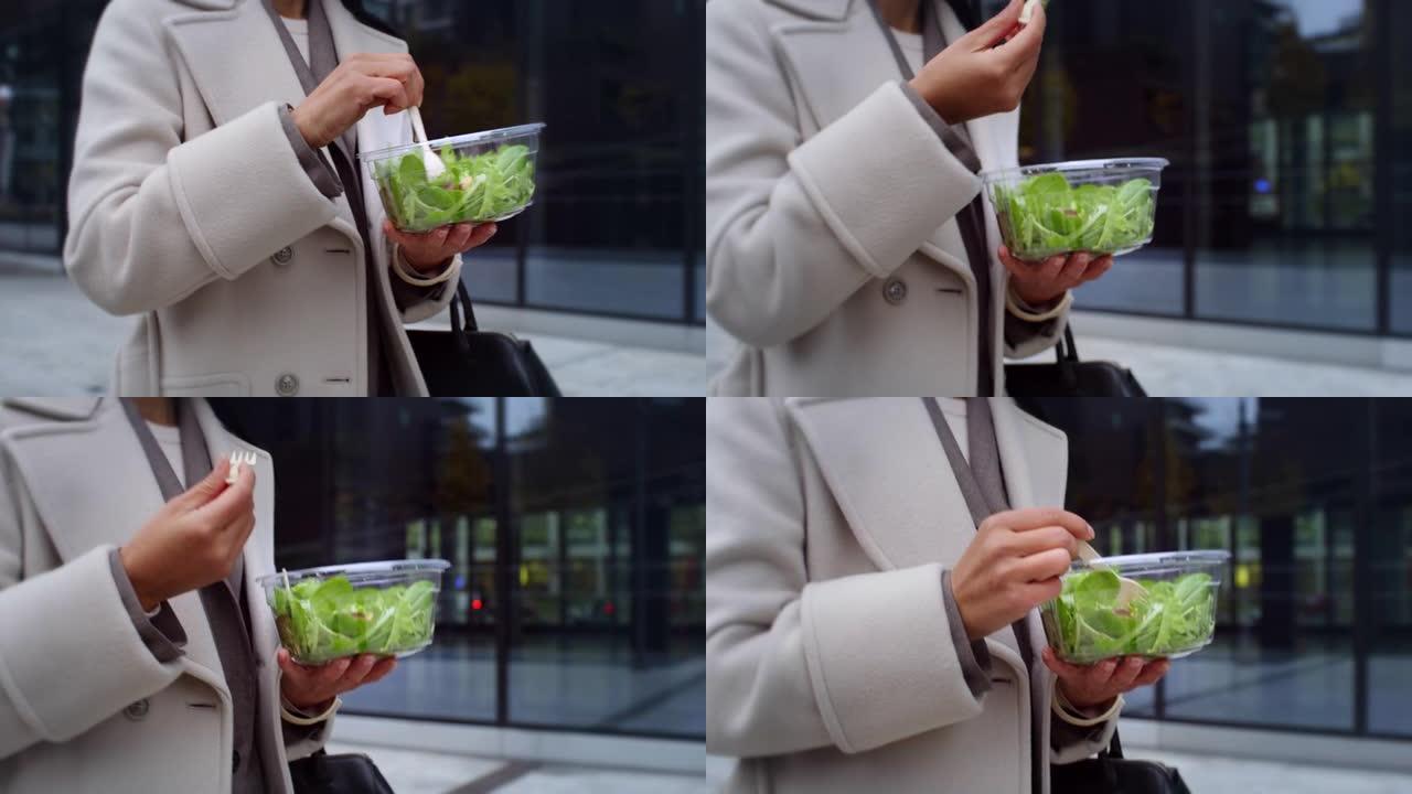近距离拍摄一位女商人一边吃沙拉一边走向她的办公室的手。素食优雅女性以健康的饮食和生活方式开始她的一天