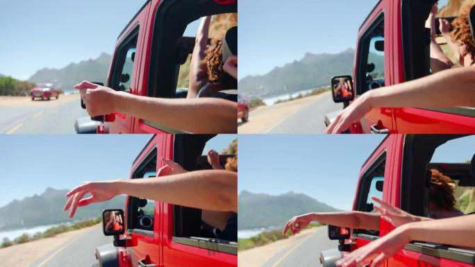 一群大笑的女性朋友在公路旅行中通过敞开车的侧窗挥舞
