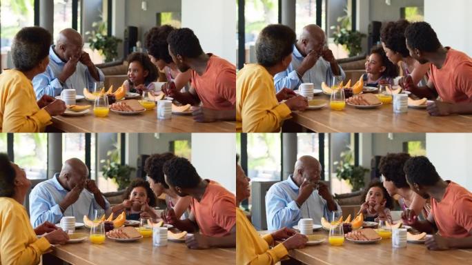 家庭与祖父母的父母和孙女在早餐时在家里的餐桌旁拉脸