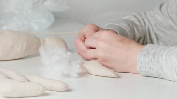 视频制作毛绒玩具，制作爪子和身体，在桌子上装满棉花。特写裁缝裁缝手