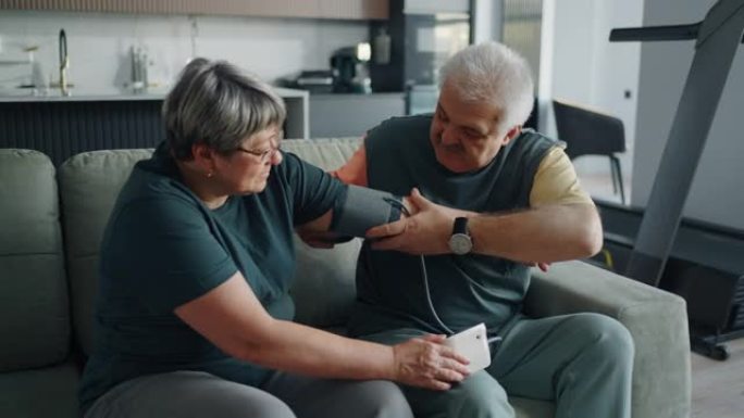 老年男子使用现代血压计将血压袖带戴在年迈的妻子的手臂上