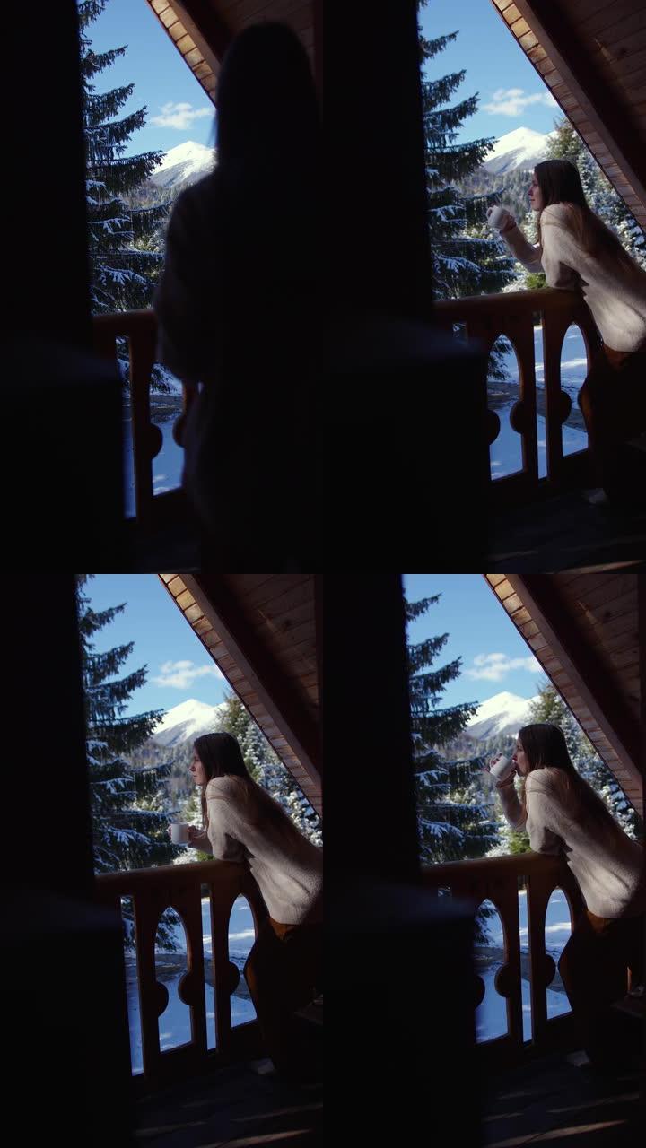 美丽的女孩带着一杯咖啡在木屋的阳台上出门。女孩在雪山和森林的背景下喝咖啡。冬天在森林里喝茶。垂直视频