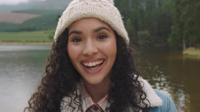 肖像美丽的混血儿女人笑着，看起来很开心，戴着便帽，在大自然的湖边享受寒冷的冬天，真实的人4k
