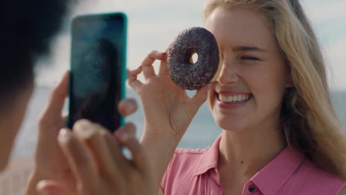 美丽的女人在海滩上与甜甜圈合影最好的朋友在社交媒体上使用智能手机分享周末在海边拍照享受夏季乐趣4k