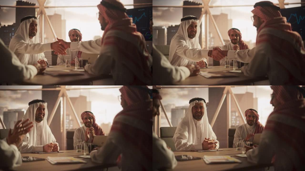 穆斯林商人在公司现代办公室完成业务交易。两个穿着传统服装的男人握手，庆祝成功的伙伴关系。沙特，阿联酋
