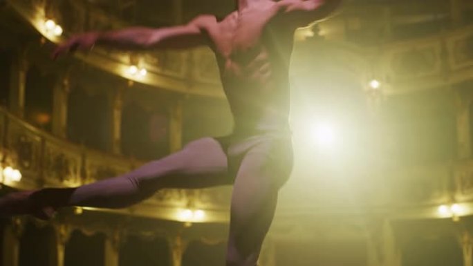 在戏剧性的灯光下，年轻的运动男子在剧院舞台上跳舞和排练旋转木马的身体特写。优雅的古典芭蕾舞男舞者为演