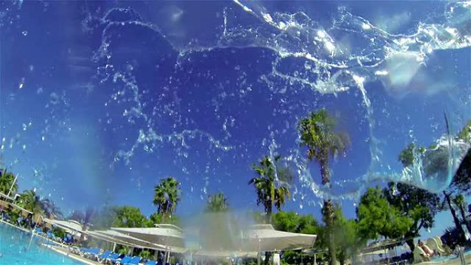 喷射水雾落在游泳池里。背景-游泳池和棕榈树。