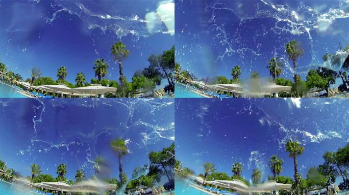喷射水雾落在游泳池里。背景-游泳池和棕榈树。