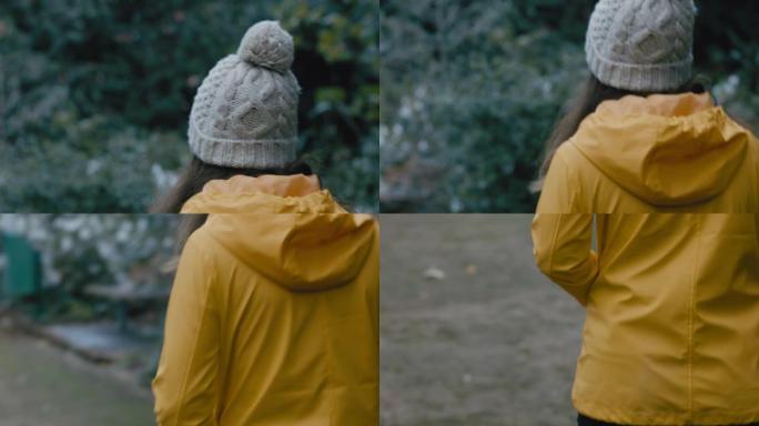 阴天穿着黄色夹克在公园散步的后视年轻女子享受大自然