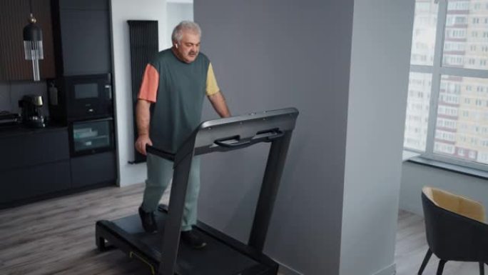 老年男子在跑步机上训练，在家通过入耳式耳机听音乐，健身锻炼
