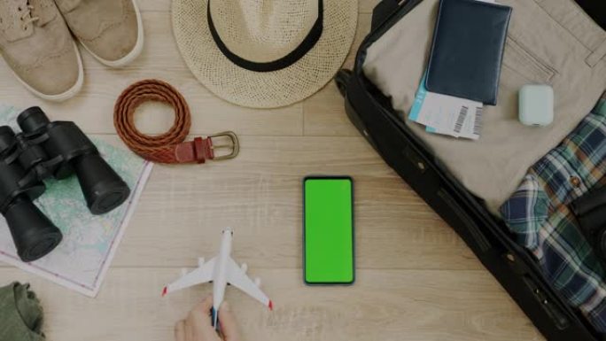玩具飞机降落在打包行李箱门票和绿屏手机旁边的桌子上的放大俯视图
