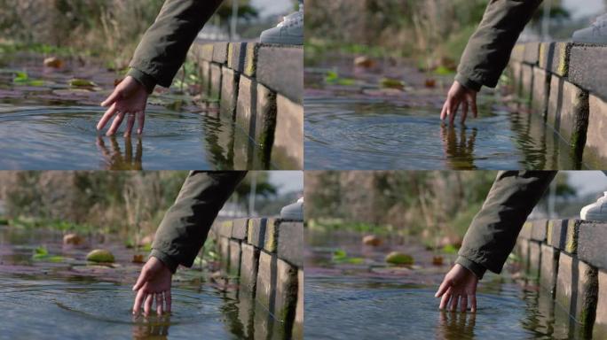 特写女人手泼水享受触摸室外自然公园的新鲜池塘