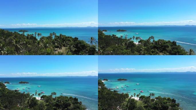 空中展示在美丽的海滩上的棕榈树上方拍摄，海水绿松石色，停泊的旅游船和游艇。在天堂岛度假