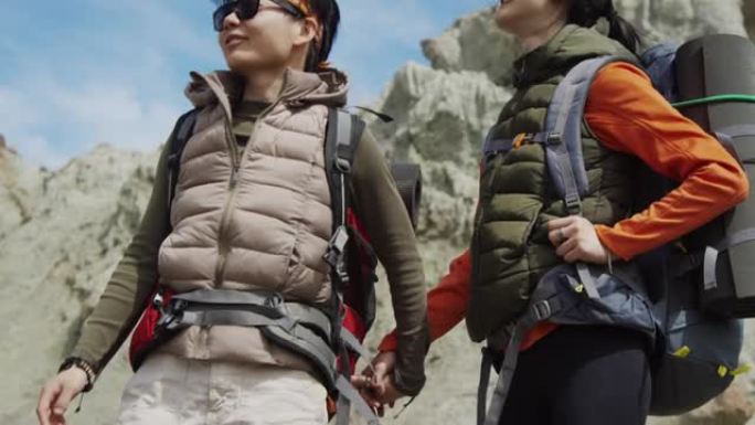 两个亚洲女性朋友牵着手，环顾岩石底部